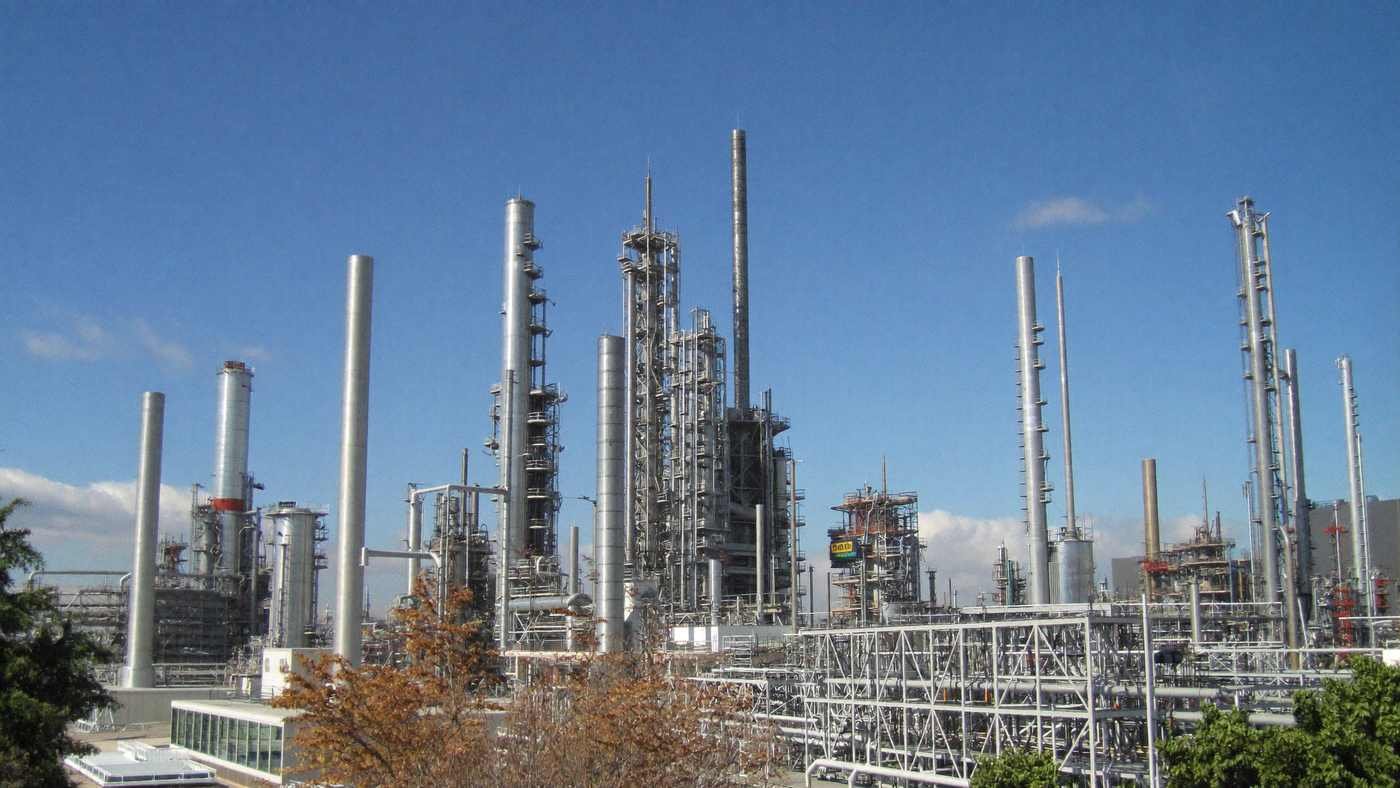 Complexo petroquímico com torres de destilação de aço sob céu azul, em dia ensolarado