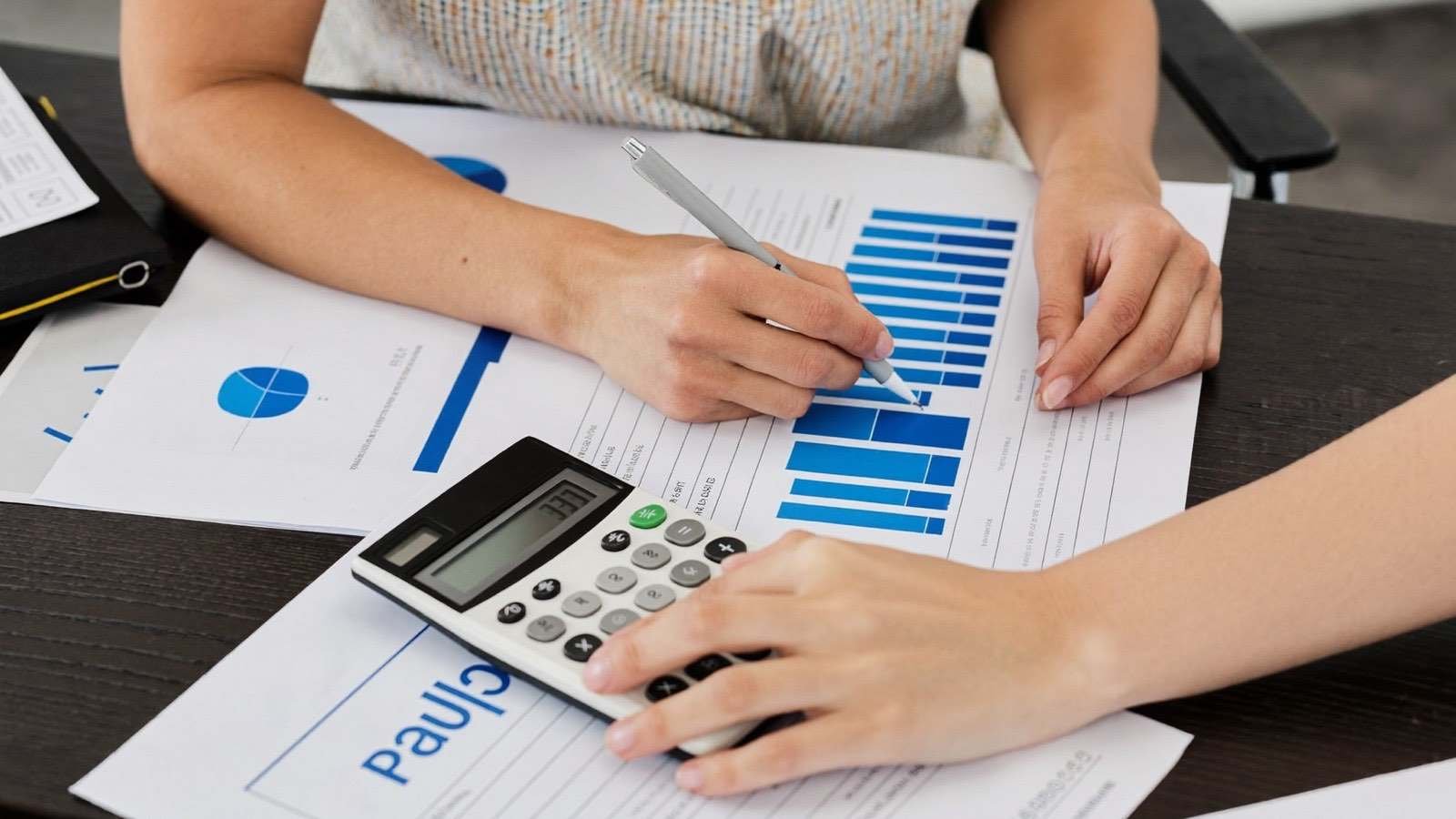 Mãos analisando gráficos financeiros com calculadora sobre a mesa