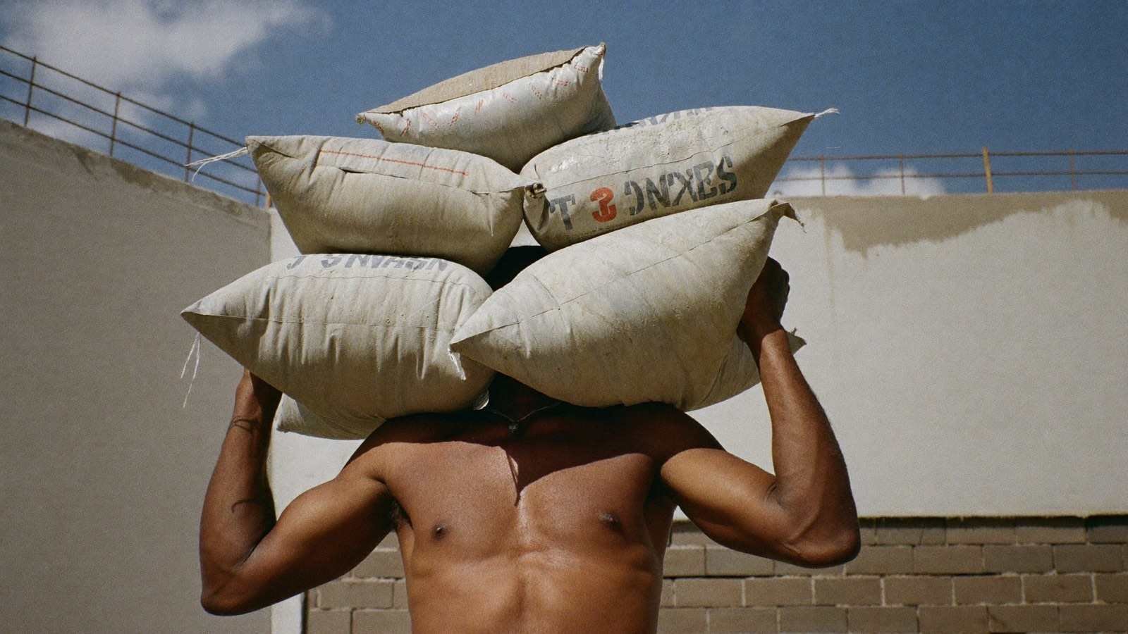 Trabalhador carregando sacos de cimento pesados em canteiro de obras