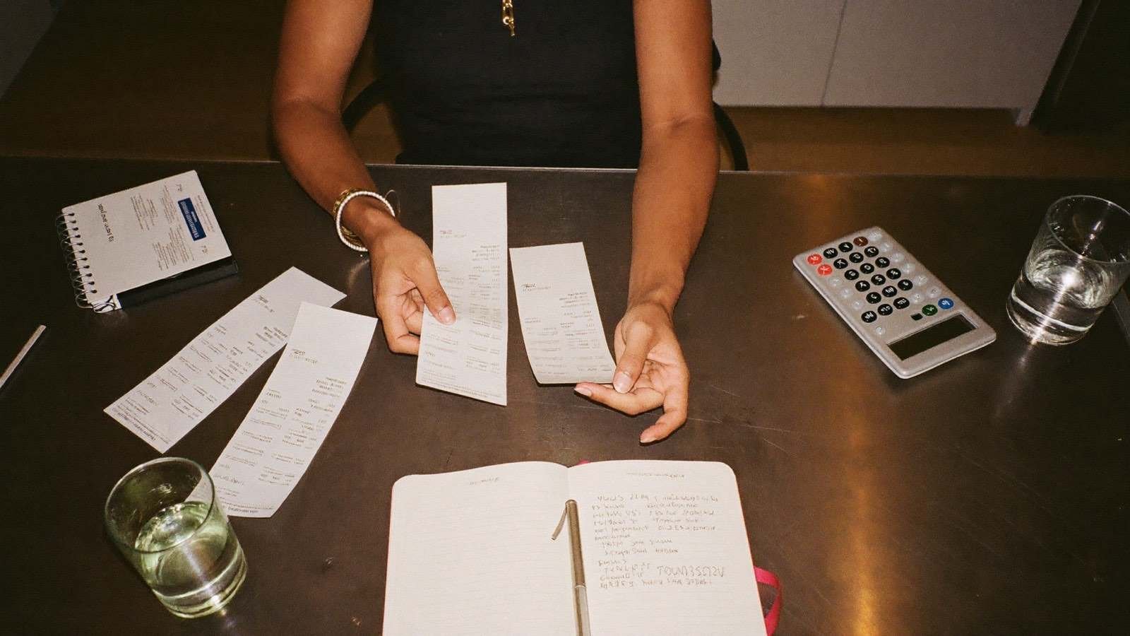 Pessoa conferindo notas fiscais e orçamento doméstico na mesa da cozinha