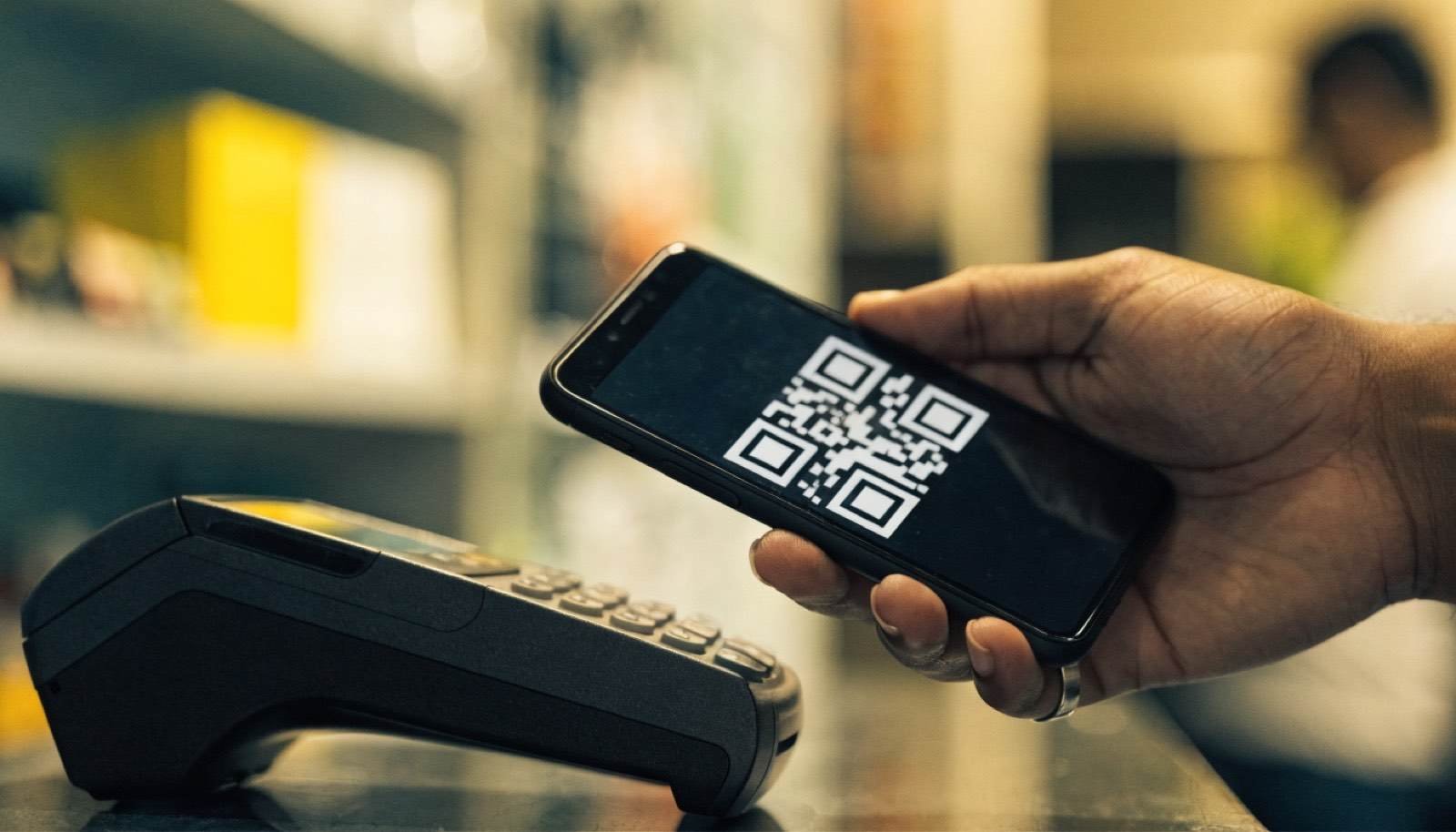 Celular exibindo QR Code de pagamento sendo aproximado de maquininha