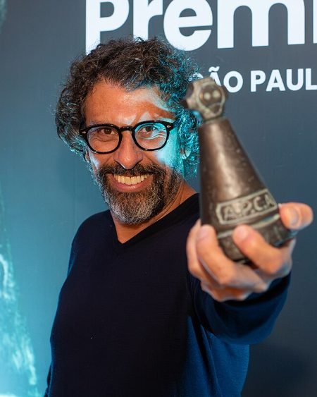 Milhem Cortaz sorrindo com troféu do Prêmio APCA (Foto: amigosdaarte/Wikimedia Commons, domínio público)