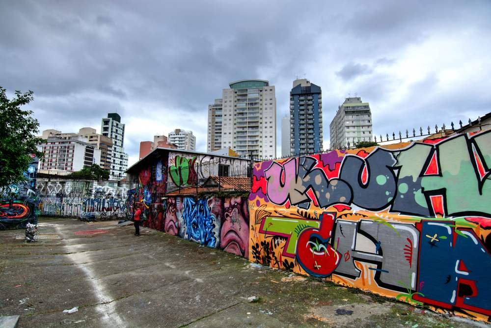 Beco grafitado na Vila Madalena, com prédios da região ao fundo (Foto: Slyronit/Wikimedia Commons, CC BY-SA 4.0)
